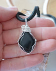 Black onyx necklace for men in hand for size reference – natural black crystal, silver copper wire, flat black leather cord, July birthstone.