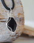 Right angle close-up of men's black onyx necklace – detailed silver copper wire wrapping, raw onyx, flat black leather cord.