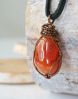 Left angle close-up of men's carnelian necklace – highlighting unique wire-wrapped artistry, orange carnelian, black leather cord.