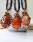 hree raw carnelian pendants for men – showing natural variation in size, shape, and orange shade, black leather cord.