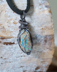 Right angle close-up of men's opal necklace – detailed antiqued sterling silver wire wrapping, raw opal, black leather cord.