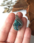 Peacock ore pendant in hand for size reference – natural raw bornite, white gold copper wire wrapping, Capricorn and Cancer birthstone, masculine design.