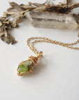Raw peridot necklace for women on gold plated brass chain, flat lay – artisan gold copper wire wrapping, natural August birthstone pendant.