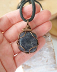 Sapphire pendant for men in hand for size reference – genuine raw sapphire, bronze copper wire, black leather cord, September birthstone.