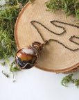 Handcrafted raw sardonyx necklace laying flat – artisan bronze and dark silver copper wire wrapping, August birthstone jewelry for all genders, Designs by Nature Gems.