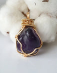 Front side angle of women’s gold amethyst necklace, polished dark amethyst pendant, artisan gold plated copper wire wrap