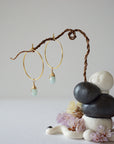 Angled view of gold plated aquamarine hoop earrings with wire wrapped gemstone drops, showing faceted March birthstone detail