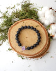 Top view of black lava stone bracelet with raw amethyst centerpiece and pyrite accents on stretch cord