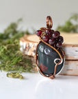 Detailed side view of a bloodstone pendant showing antique bronze and tin plated copper wire wrapping with garnet accents