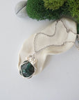 Handmade silver wire wrapped emerald and freshwater pearl necklace laying flat on a silver plated chain, artisan jewelry for women