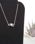 Focused left-side close-up of sterling silver emerald and pearl bar necklace on jewelry display