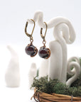 Side angle of garnet drop earrings on a display stand, highlighting antique bronze copper wire wrapping.