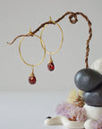 Angled view of gold plated garnet hoop earrings with wire wrapped gemstone drops, showing faceted January birthstone detail
