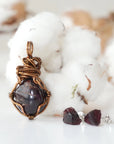 Back view of a wire wrapped garnet pendant and side view of garnet stud earrings in a women’s jewelry set