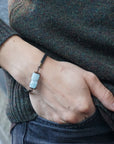 Men's aquamarine bracelet with faceted aquamarine stones, antique bronze wire, and black leather cord on male model's wrist, Designs by Nature Gems