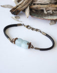 Top view of men's aquamarine bracelet, showing faceted aquamarine stones, antique bronze wire wrapping, and black leather cord
