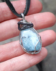 Aquamarine pendant in hand for size reference, genuine polished raw aquamarine, black and white gold finish wire wrapping