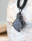 Left-angle close-up of raw sapphire pendant revealing the precision of antiqued sterling silver wire-wrapping craftsmanship — men's artisan crystal jewelry
