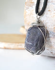 Left-angle close-up of natural sapphire pendant revealing the precision of dark silver wire-wrapping craftsmanship — men's artisan crystal jewelry