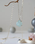 Minimalist aquamarine necklace hanging on display, detailed front view, genuine gemstone in 925 sterling silver claw setting, Designs by Nature Gems