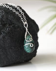 Right angle detail of minimalist emerald pendant for women with natural faceted teardrop emerald and sterling silver wrapping