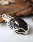 Side angle of wire wrapped garnet pendant showing detailed silver plated copper wrap and raw crystal texture