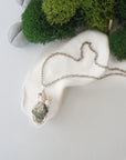 Handmade silver wire wrapped peridot and freshwater pearl necklace laying flat on a silver plated chain, artisan jewelry for women