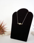 Left angle view of peridot and pearl bar necklace in 925 sterling silver on jewelry display