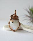 Front angle view of natural rainbow moonstone pendant with detailed antique bronze and dark silver wire wrapping