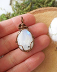 Natural rainbow moonstone pendant shown in hand for size reference with handcrafted antique bronze finish over copper wire wrapping