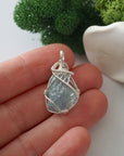 Handmade raw aquamarine pendant held in hand showing size — natural pale blue aquamarine stone wire wrapped in 925 sterling silver, 8-10 carats, one of a kind