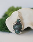 Back view of raw emerald pendant showing detailed artisan wire wrapping in soft silver copper.