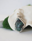 Side angle detail of natural emerald pendant highlighting intricate artisan wrapping in soft silver copper wire.