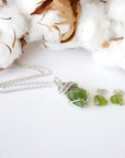 Raw peridot necklace and stud earring set for women on flat surface — 925 sterling silver chain and wire wrapped pendant with matching earrings, August birthstone crystal jewelry