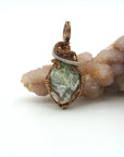 Front view of raw peridot pendant for women — soft sage olive green crystal with natural surface texture, antique bronze and dark silver wire wrap, handcrafted August birthstone jewelry