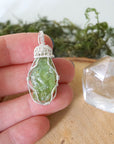 Raw peridot pendant for women held in hand for size reference — natural olive green crystal in 925 sterling silver wire wrap, handcrafted August birthstone jewelry