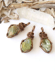 Three raw peridot pendants for women showing natural variation in size, shape, and olive green colour — handcrafted antique bronze wire wrapped August birthstone necklaces