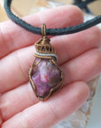 Raw ruby pendant held in hand to show size — natural ruby stone in two-tone bronze and silver wire wrapping, men's handmade crystal necklace