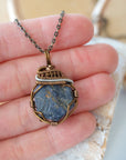 Raw sapphire pendant held in hand to show size — wire wrapped in antique bronze and dark silver, handcrafted crystal necklace by Designs by Nature Gems