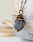 Left-angle close-up of raw sapphire pendant revealing the dual-metal wire-wrapping craftsmanship in antique bronze and dark silver
