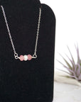 Focused left-side close-up of sterling silver ruby and pearl bar necklace on jewelry display