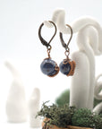 Side angle of sapphire drop earrings on a display stand, highlighting antique bronze copper wire wrapping.