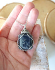 Natural sapphire pendant held in hand to show size — dark silver wire wrap on white gold plated chain, handcrafted crystal necklace by Designs by Nature Gems