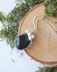 Handmade silver wire wrapped shungite and freshwater pearl necklace laying flat on a silver plated chain, artisan jewelry for women