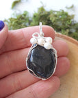 Shungite and freshwater pearl pendant necklace in hand for size reference, silver wire wrapped, handcrafted gemstone jewelry