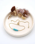 Handmade turquoise bracelet displayed on ceramic tray showing natural blue-green crystals and gold chain - December birthstone gift for her