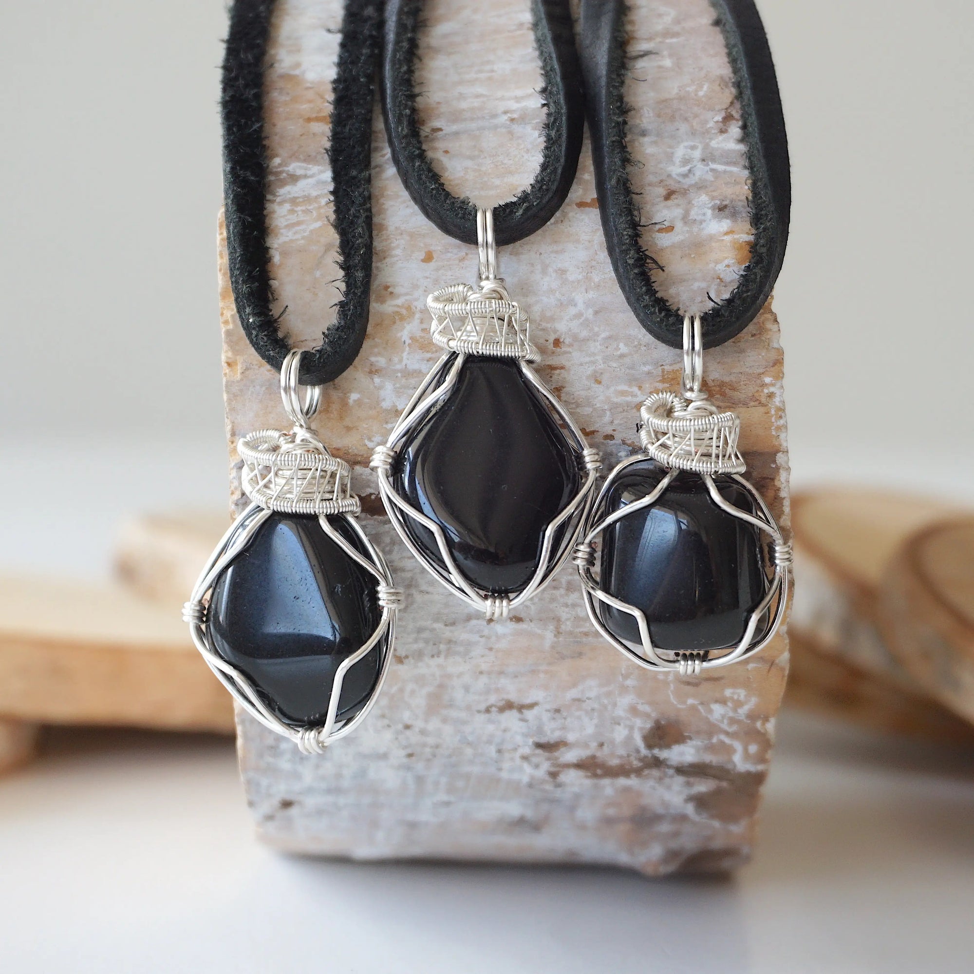 Three raw black onyx pendants for men – showing natural variation in size, shape, flat black leather cord.