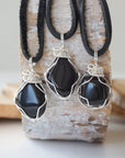 Three raw black onyx pendants for men – showing natural variation in size, shape, flat black leather cord.