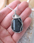 Raw black tourmaline necklace for men in hand – size reference, showcases natural black stone and artisan wire wrapping.