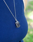 Person wearing a blue sleeveless top with a silver necklace featuring a pendant.